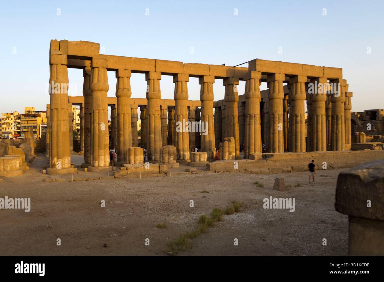 Antike Steinsäulen des Tempels Luxor, beleuchtet durch warmes Sonnenlicht in Ägypten, mit Menschen, die durch die archäologische Stätte in Ägypten laufen Stockfoto