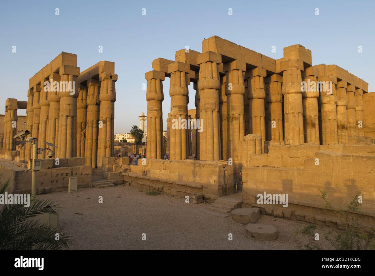 Antike Steinsäulen des Tempels Luxor, beleuchtet durch warmes Sonnenlicht in Ägypten, mit Menschen, die durch die archäologische Stätte in Ägypten laufen Stockfoto
