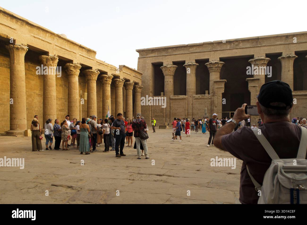 Touristen versammeln sich und machen Fotos im Innenhof des antiken Tempels von Edfu mit massiven Steinsäulen und historischer Architektur, Ägypten Stockfoto