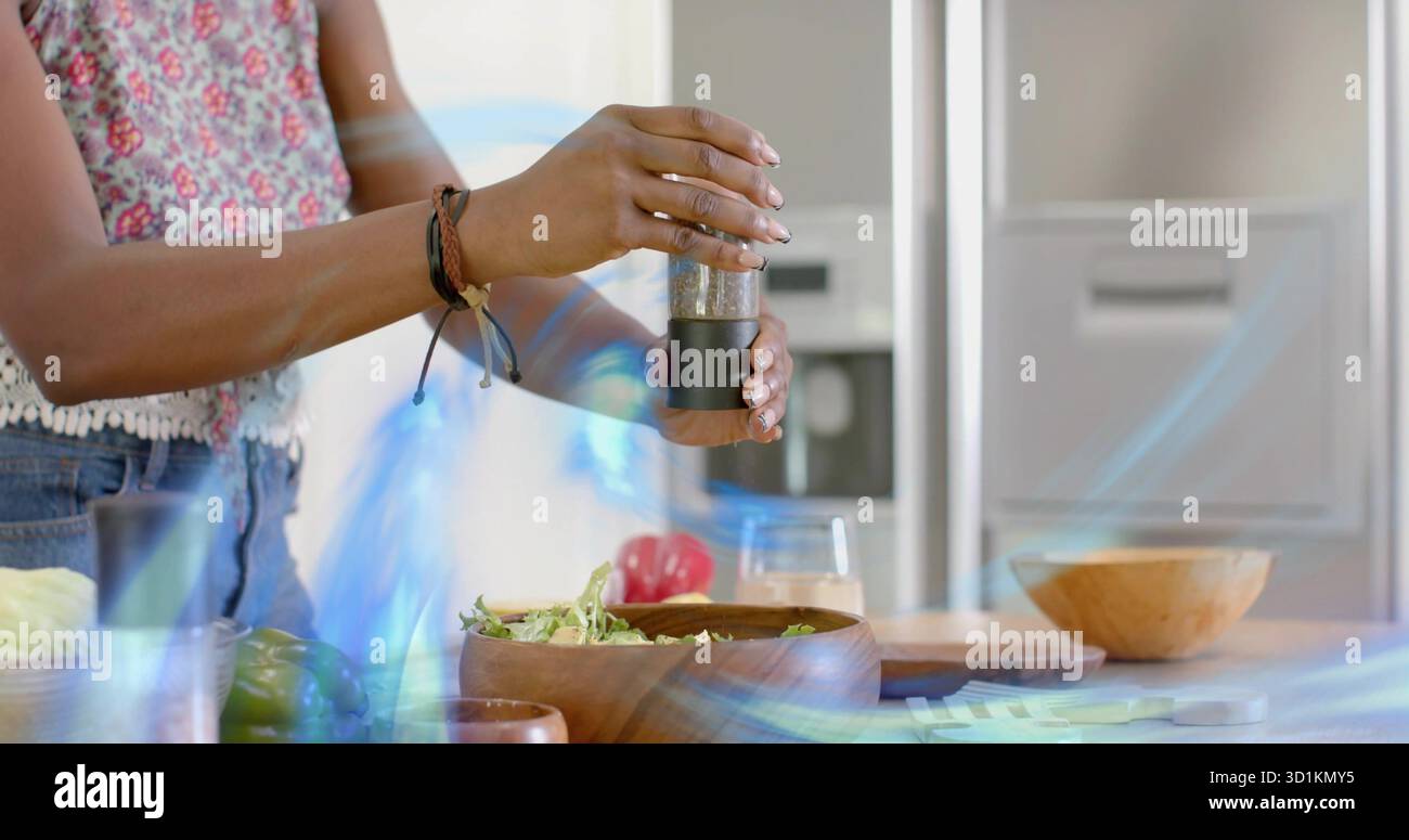 Frau würzt Salat in einer Holzschale auf der Kücheninsel, Pfeffermühle und Paprika Stockfoto