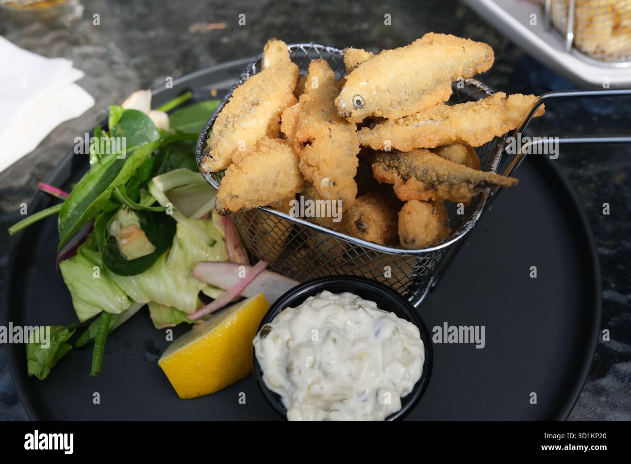 Frittierte Weißhait serviert mit Salat und Tatarsauce auf einem schwarzen Teller. Stockfoto