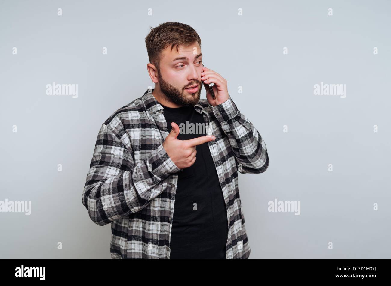 Mann in kariertem Hemd, der telefoniert und seitwärts zeigt Stockfoto