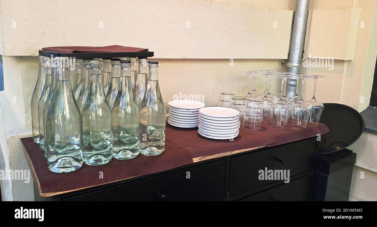 Mit Wasser gefüllte Glasflaschen, die ordentlich neben Tellern und Gläsern angeordnet sind, schaffen eine einladende Atmosphäre für eine Veranstaltung oder ein Treffen. - Smartphone-aufgenommenes Stockfoto