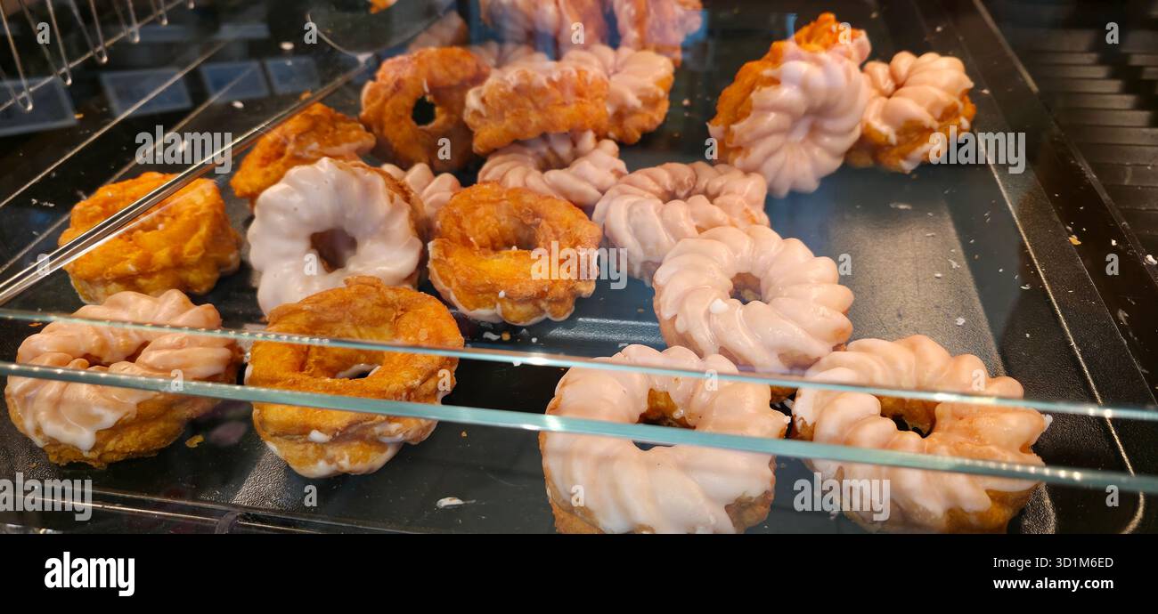Verschiedene Donuts mit Glasur und einzigartigen Formen werden in einem Glaskoffer ausgestellt und bieten verlockende Leckereien in einer Bäckerei. Stockfoto
