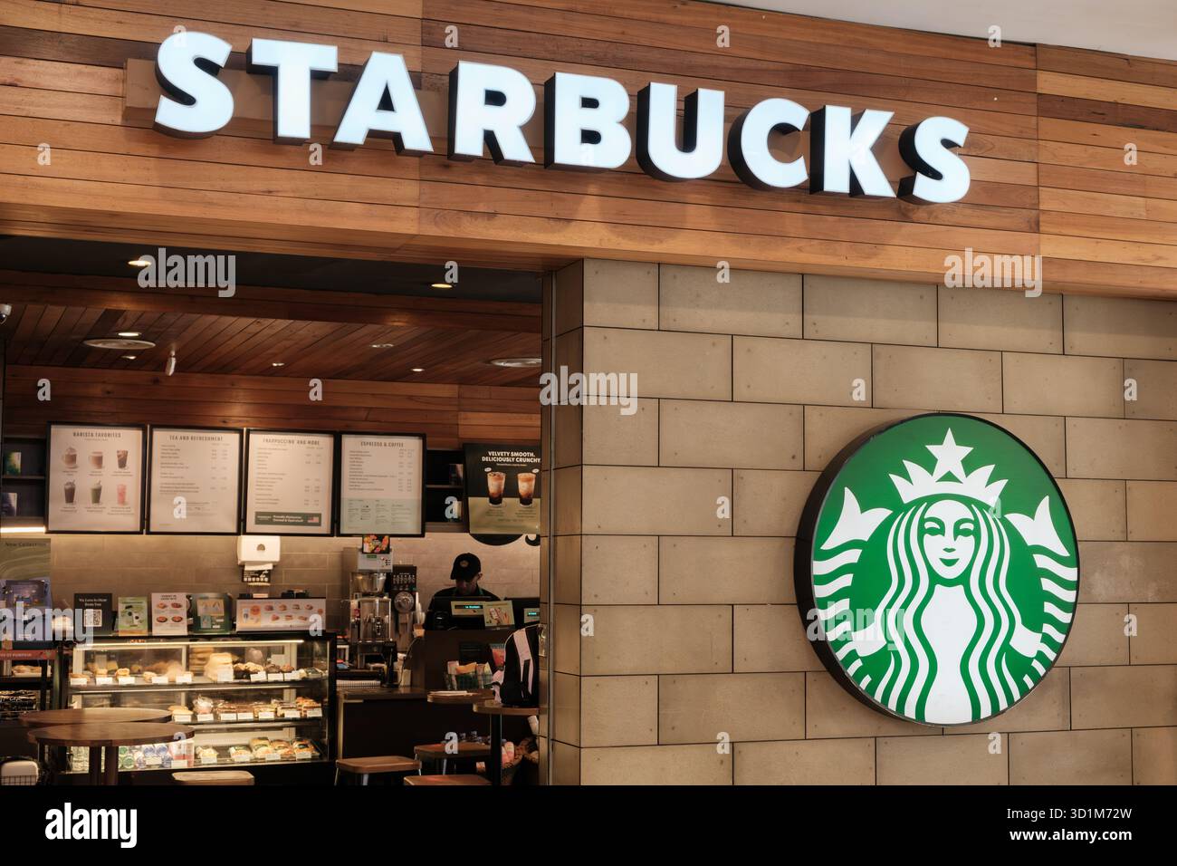 Der Café-Shop mit Starbucks Emblem ist mit einem grünen Logo an der Wand und Menüartikeln auf einem Holzinnenraum sichtbar. Stockfoto