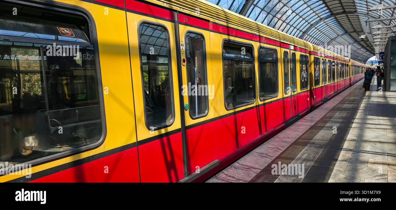 Berlin, Deutschland - 13. Mai 2025: Rot-gelbe U-Bahn parkt am Bahnsteig der Stadt mit moderner Architektur und Sonnenlicht. - Smartphone-aufgenommenes Stockfoto