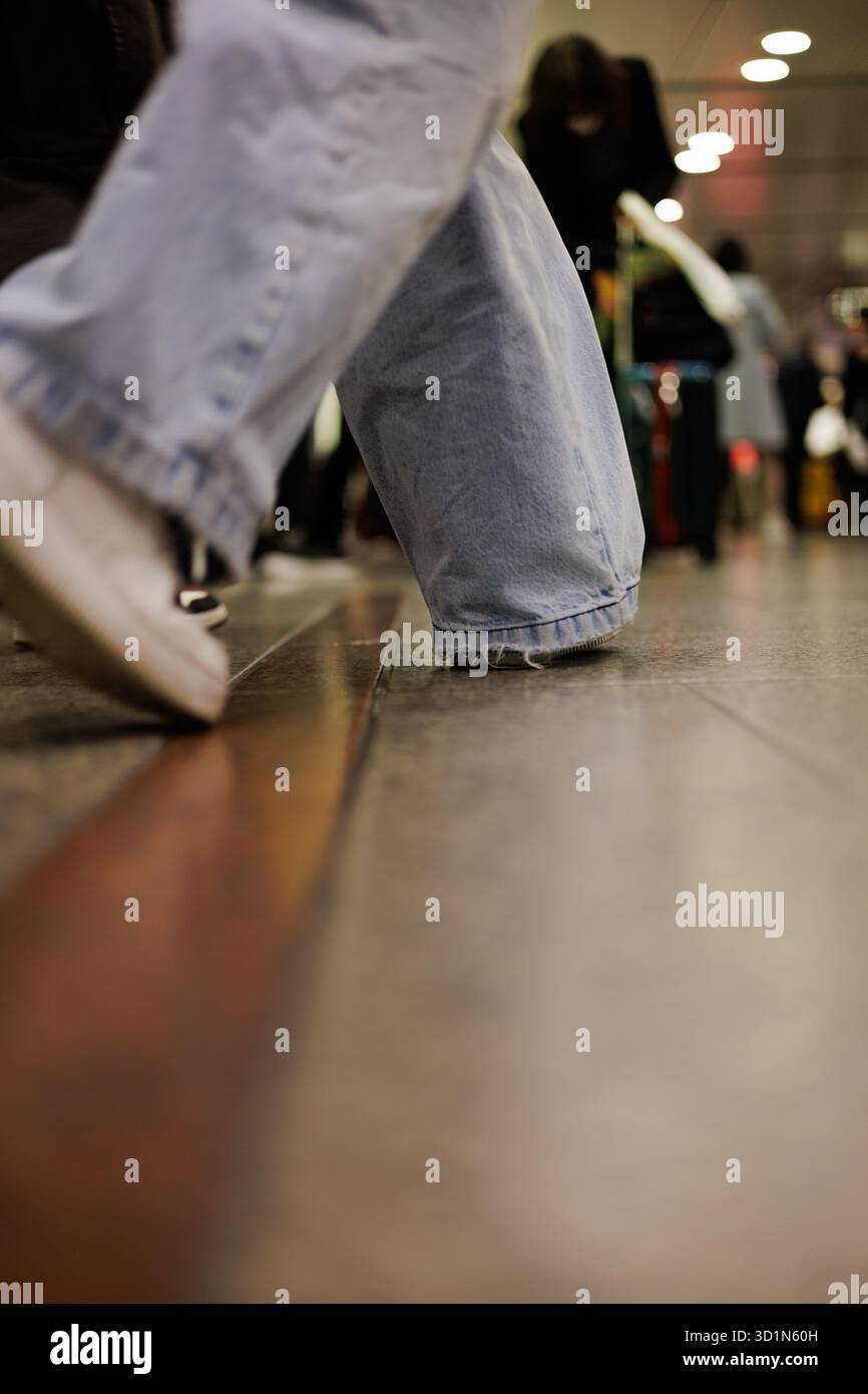 Geschäftige Menschen an belebten Orten - aus einem niedrigen Winkel sehen Sie, wie die Person lässig in weißen Turnschuhen und hellblauen Jeans durch einen überfüllten Bahnhof streift. Stockfoto