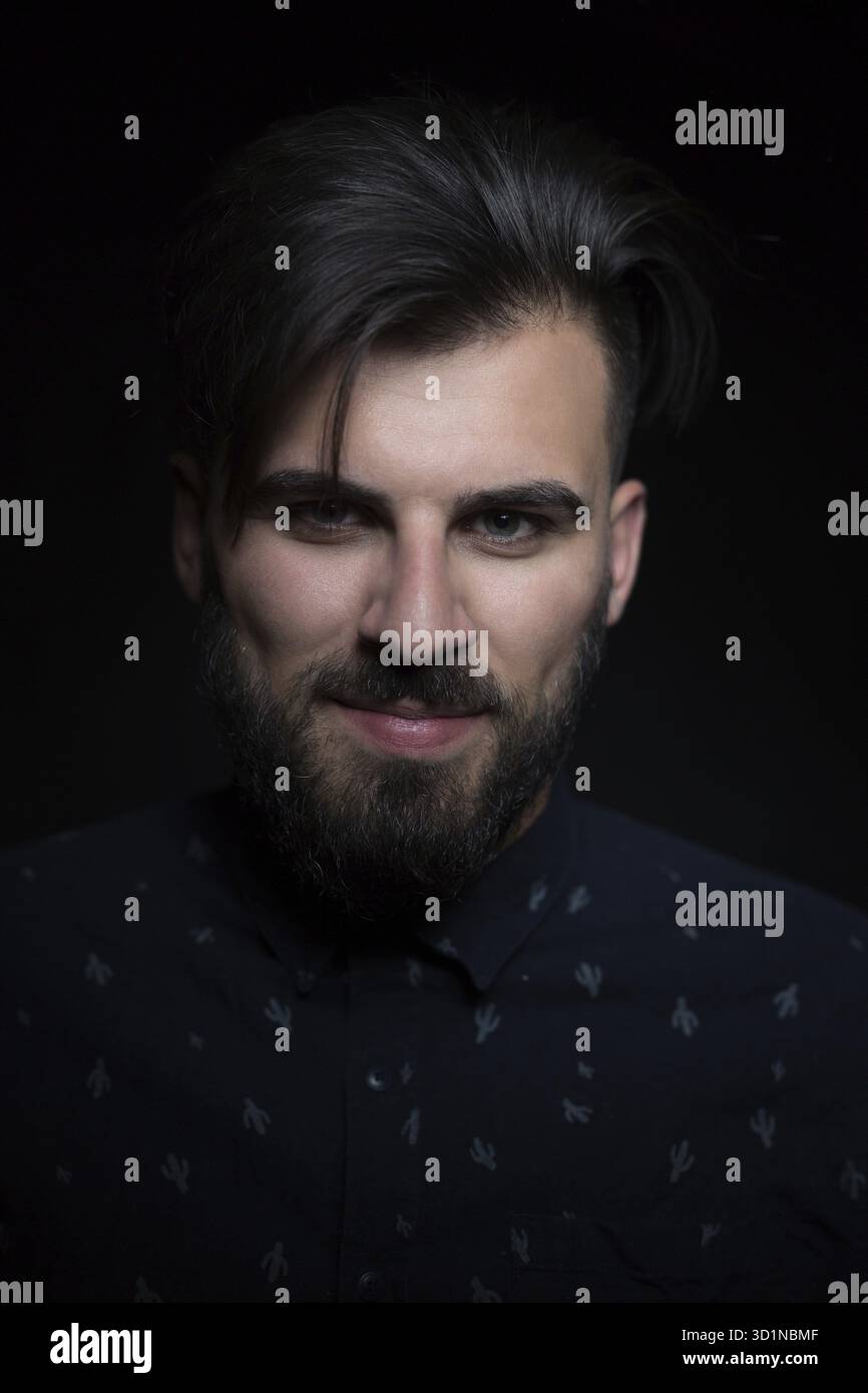 Porträt eines gutaussehenden Mannes mit schwarzem Hemd, schwarzem Hintergrund, der in die Kamera schaut Stockfoto