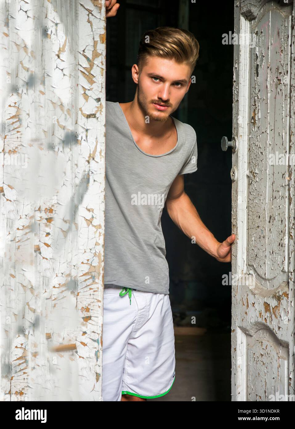 Hübscher blonder junger Mann, der die alte Tür öffnet Stockfoto