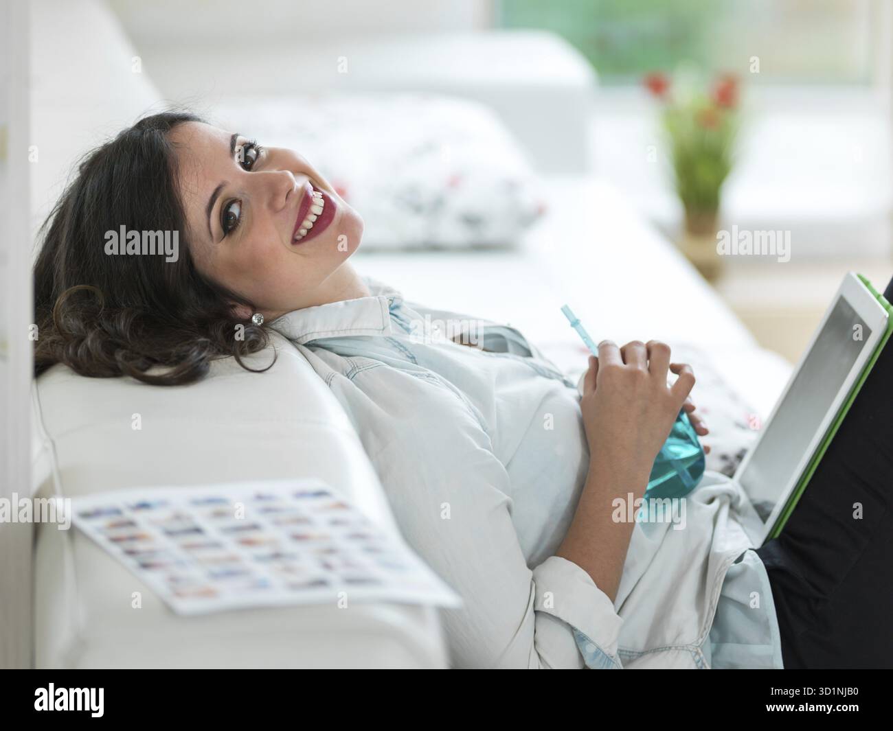 Entspannte junge Frau sitzt auf dem Sofa mit tablet Stockfoto