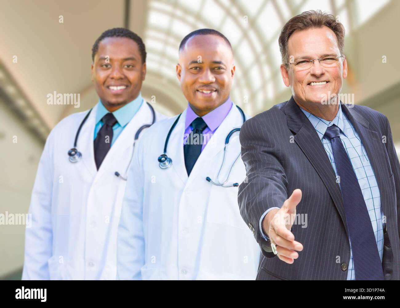 Gemischte Race Doctors hinter Geschäftsmann, der im Krankenhaus nach Handschütteln greift Stockfoto