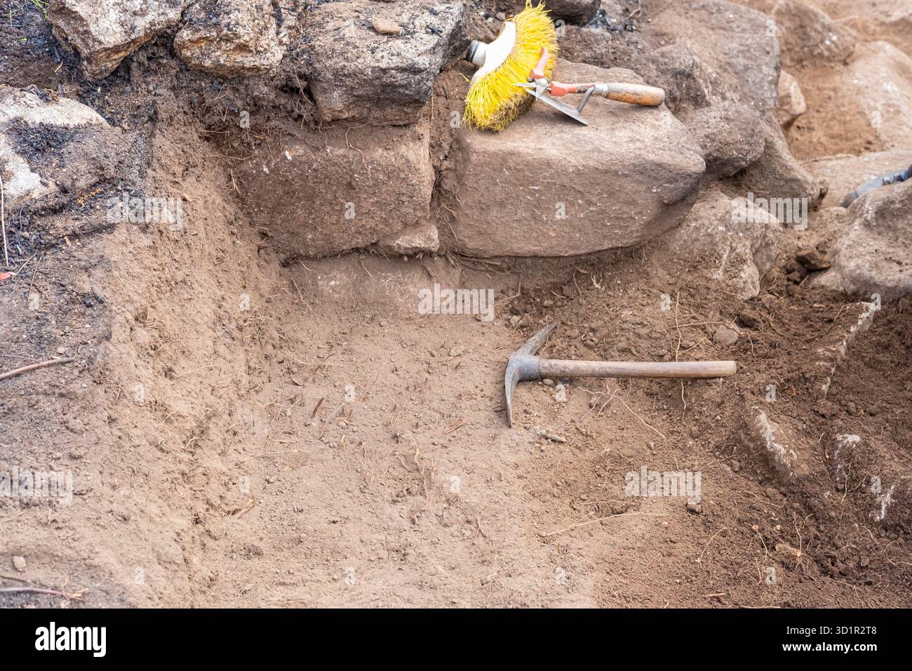 Eine Spitzhacke und eine Bürste neben einem alten Steinfundament die Werkzeuge des Handels Stockfoto
