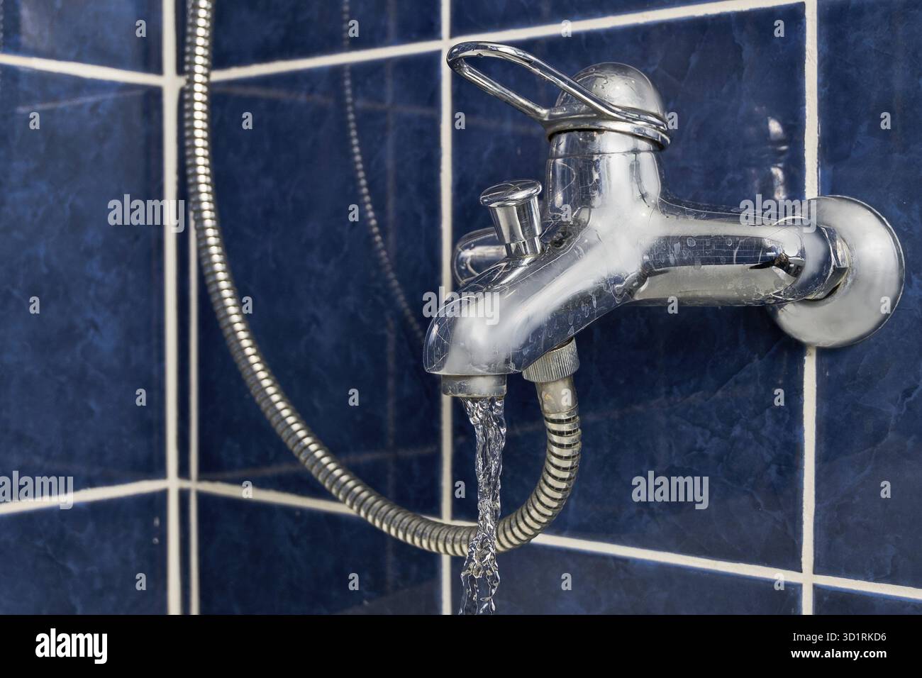 Verchromte Armaturenwinkel mit gefrorenem Wasser in der Luft, Vorderansicht auf blauer gefliester Wand, Vintage-Farbe Stockfoto