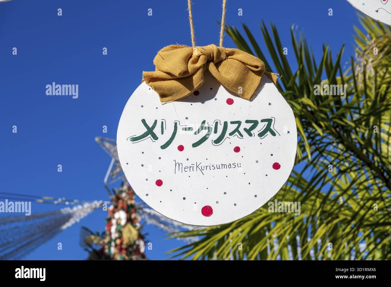 Denia, Alicante - Spanien - 22.12.2023: Hellblauer Himmel mit „Merry Christmas“-Schild in japanischem und orangefarbenem Band Stockfoto