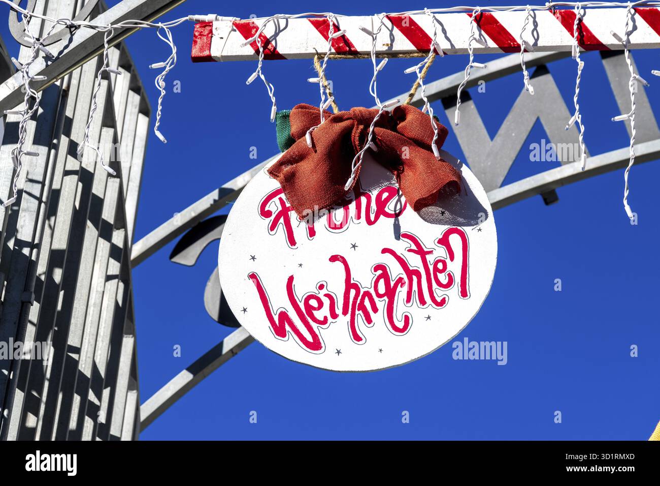 Denia, Alicante - Spanien - 22.12.2023: Hellblauer Himmel mit Weihnachtsschild „Frohe Weihnachten“ und roter Schleife Stockfoto