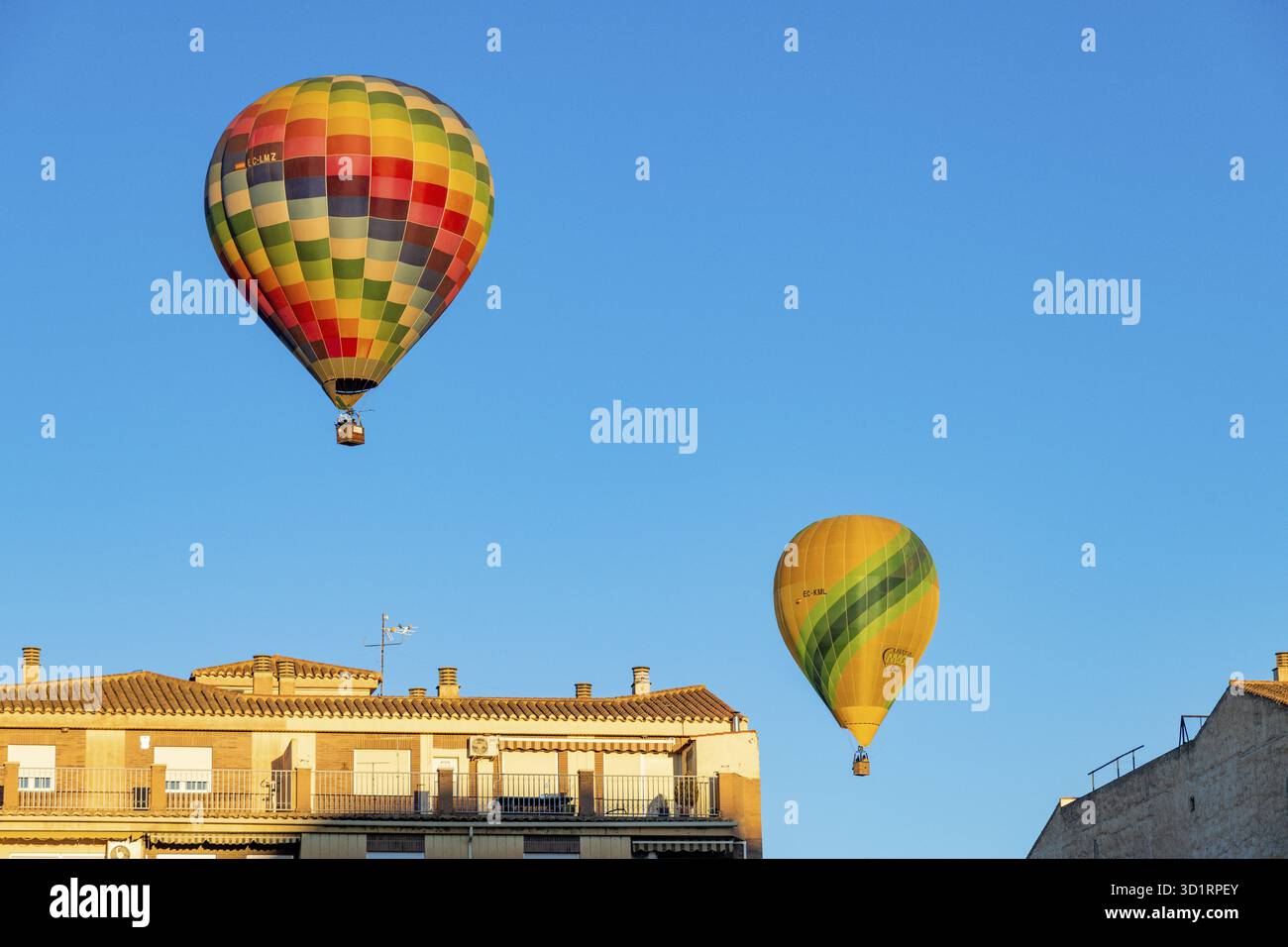 Guadix, Granada - Spanien - 24.01.2024: Zwei Heißluftballons schweben über Häusern mit roten Dächern, einer ist ein bunt karierter Ballon und der andere ist gelb Stockfoto