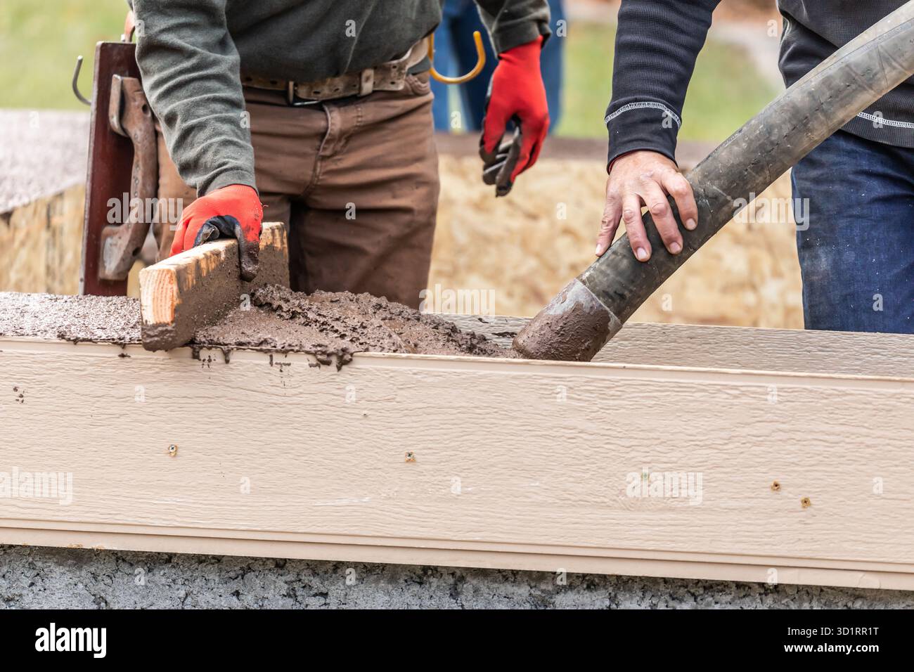 Bauarbeiter, Die Nassen Zement In Holzrahmen Gießen Und Einebnen Stockfoto