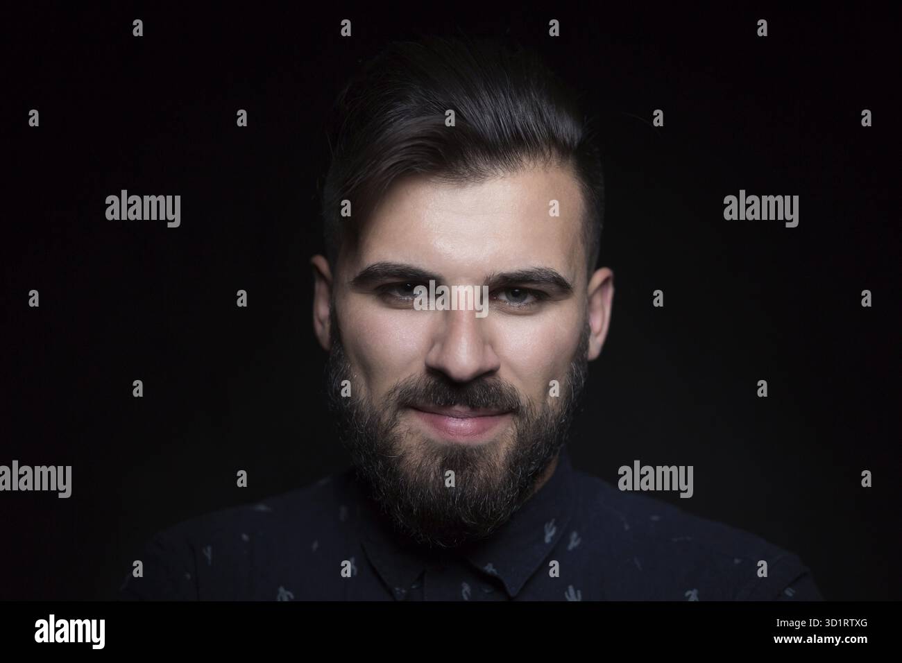 Porträt eines gutaussehenden Mannes mit schwarzem Hemd, schwarzem Hintergrund, der in die Kamera schaut Stockfoto
