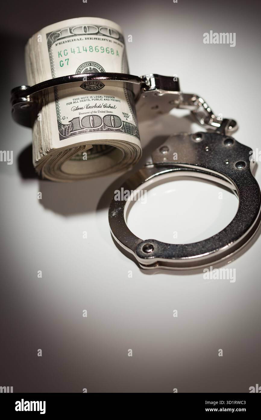 Handschellen auf Rolle von 100 Dollar-Scheinen unter Spotlight Stockfoto