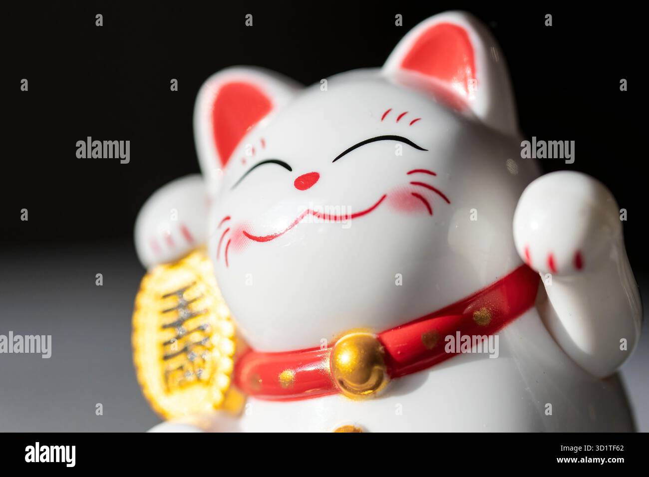 Madrid, Spanien, 25.09.2025: Nahaufnahme einer japanischen Maneki Neko Lucky Cat Figur mit rotem Kragen und Goldmünze auf dunklem Hintergrund Stockfoto