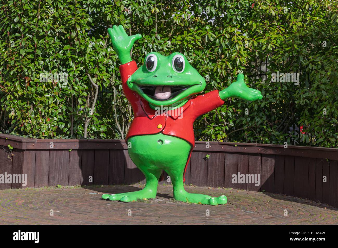 Eine einladende Statue von Rick dem Frosch, mit weit geöffneten Armen und einem großen Lächeln begrüßt Besucher in einer sonnigen Gegend von Duinrell vor einer üppig grünen Hecke Stockfoto