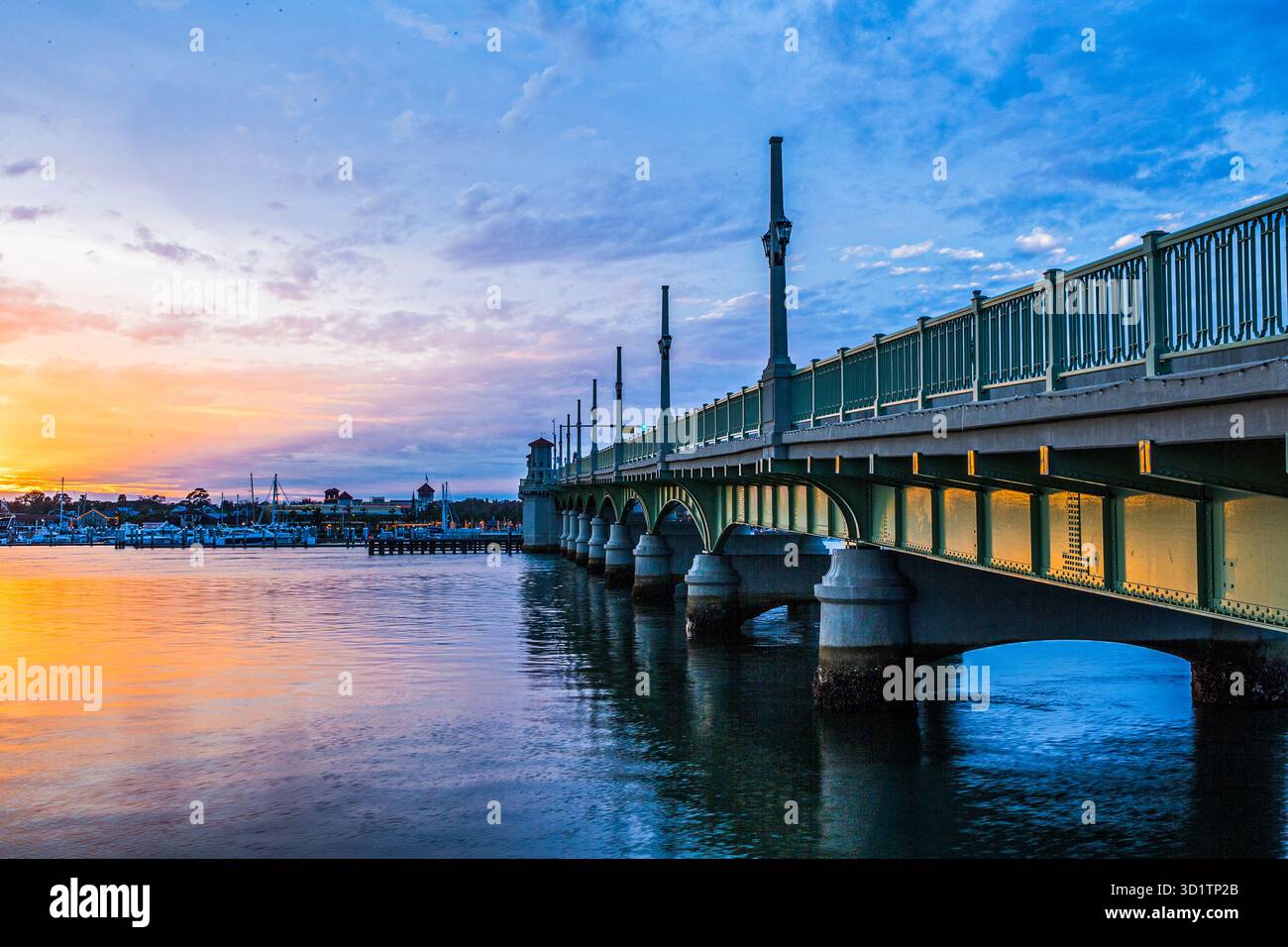Ein lebhafter Sonnenaufgang beleuchtet den Yachthafen im historischen St. Augustine, Florida, und lässt warme Reflexe auf das ruhige Hafenwasser strahlen. Segelboote und Yachten Stockfoto