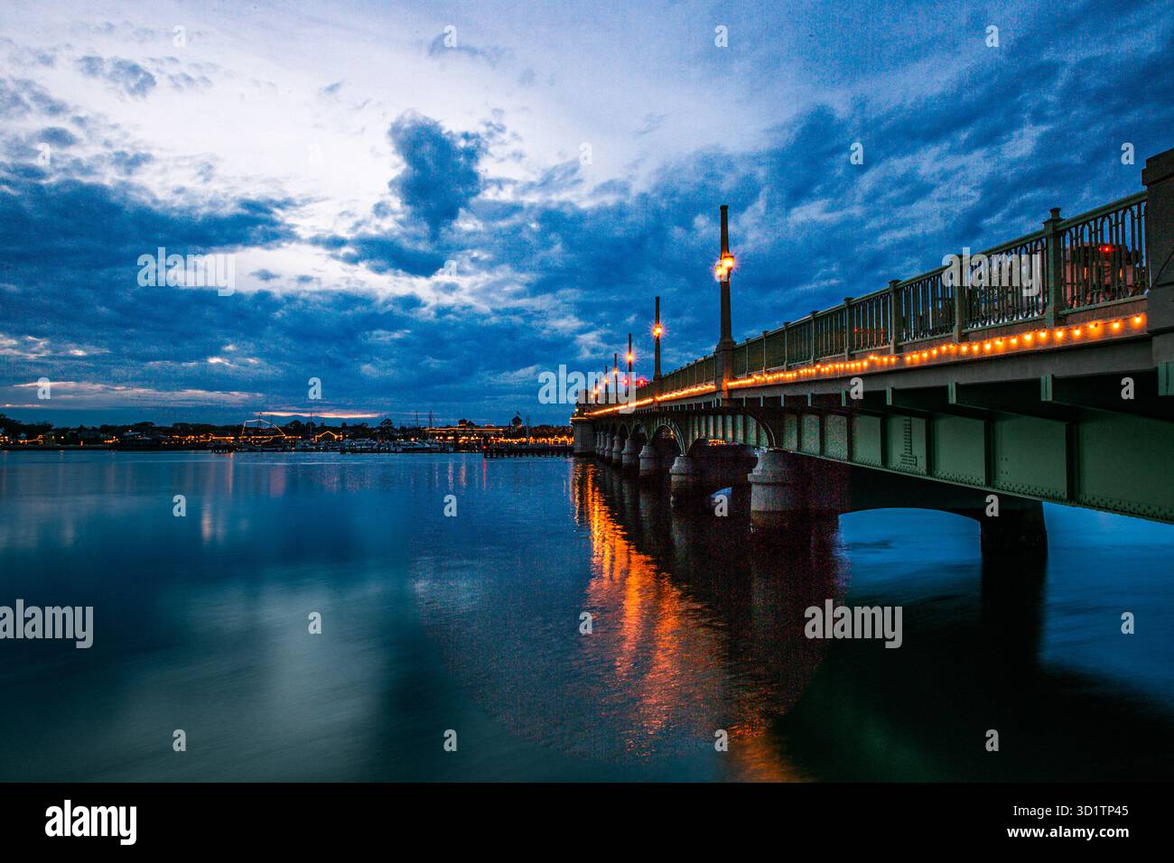 Die Bridge of Lions in St. Augustine, Florida, leuchtet mit Lichtern und warmen Straßenlaternen unter einem dramatischen blauen Stundenhimmel. Stockfoto