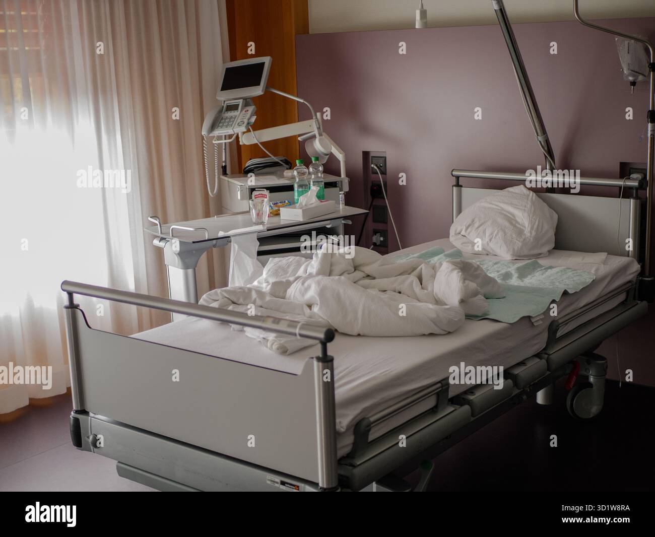 Leeres Krankenhausbett im Aufwachraum mit medizinischer Ausrüstung, Monitor und sanftem Tageslicht durch Vorhänge, Gesundheits- und Behandlungskonzept, pro Foto. Stockfoto