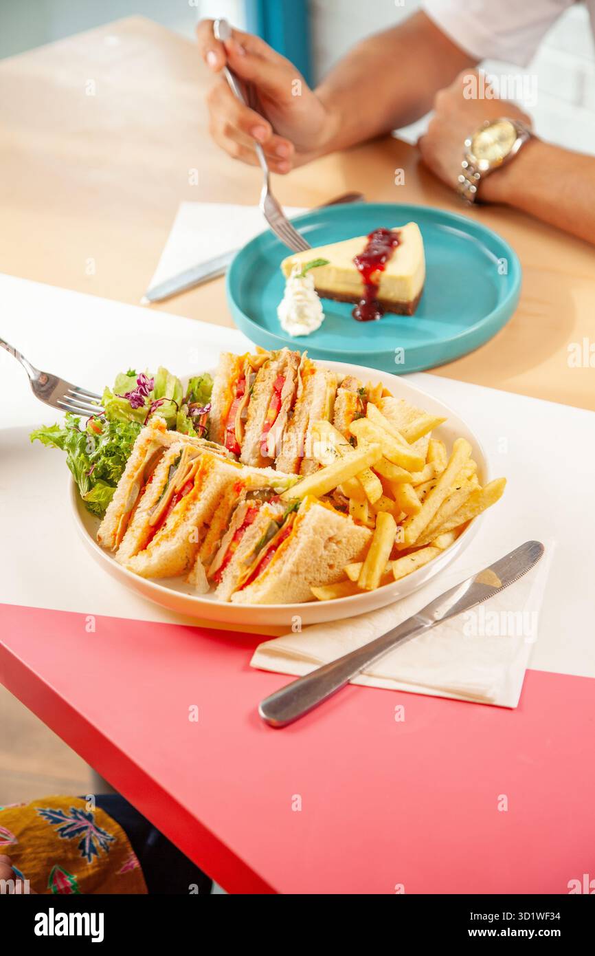 Männliche und weibliche Freunde genießen Club-Sandwich und Dessert in einem Restaurant-Café. Stockfoto