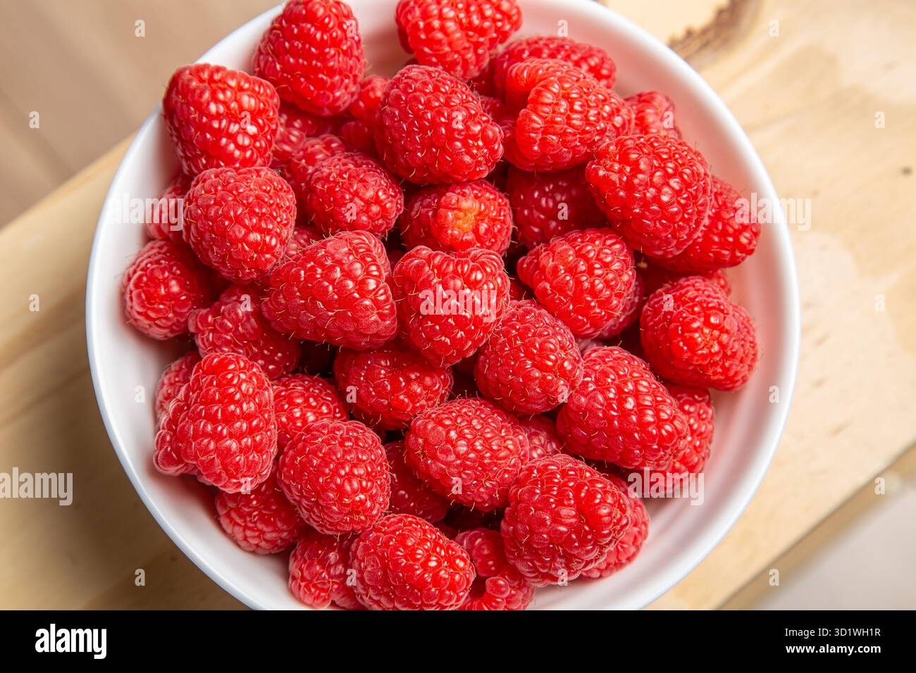 Ansicht von oben nach unten, die den Rahmen füllt, von frischen, leuchtend roten Himbeeren in einer weißen Schüssel Stockfoto