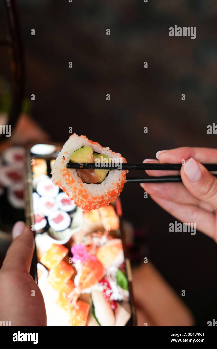 Sushi-Roll mit Avocado und Lachs in Stäbchen Stockfoto