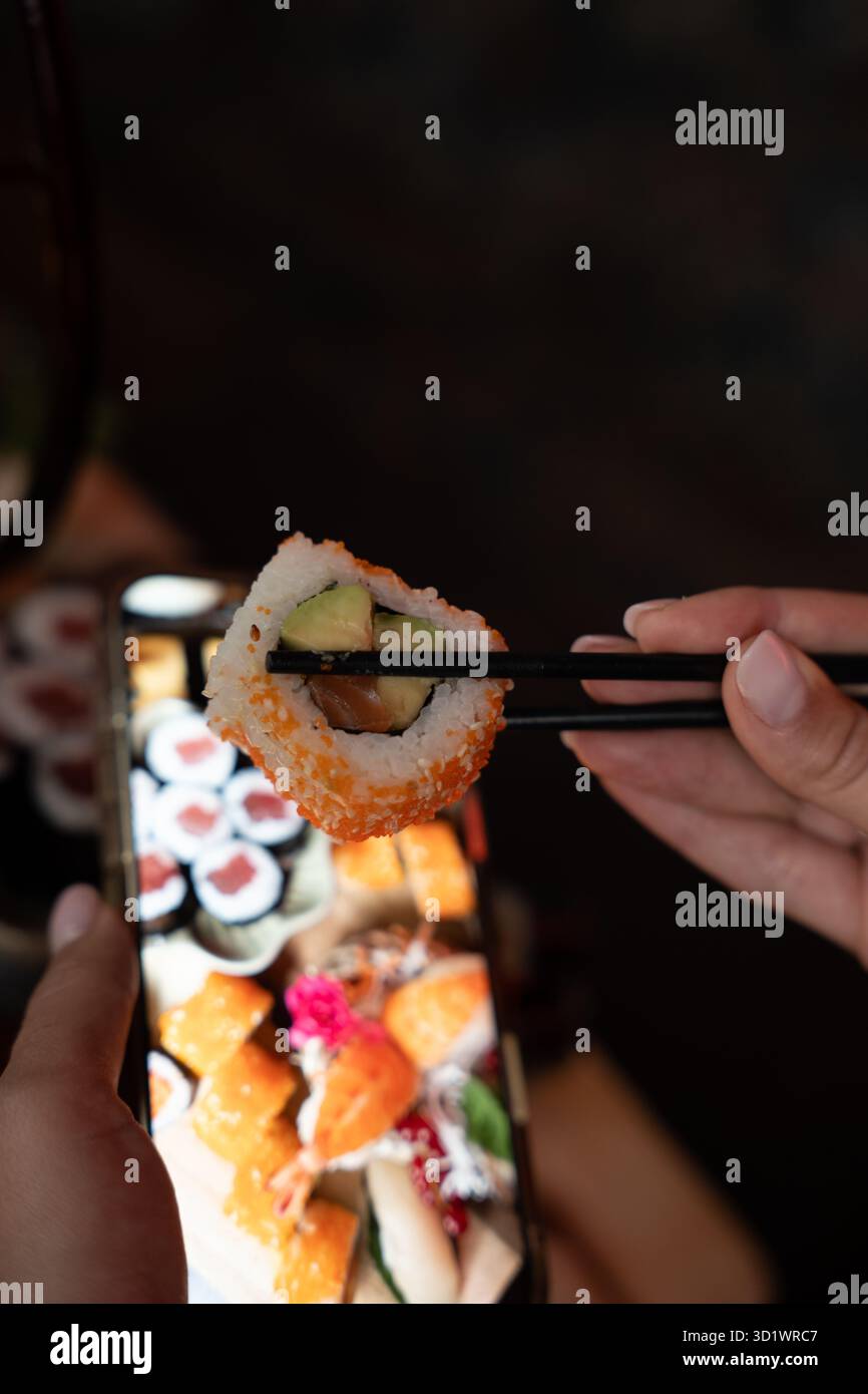 Sushi-Roll mit Avocado und Lachs in Stäbchen Stockfoto