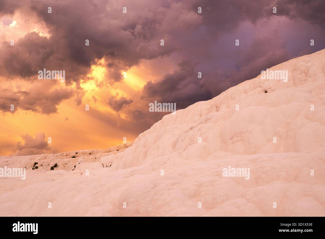 Sonnenuntergangslicht bricht durch Sturmwolken über den weißen Terrassen von Pamukkale, Türkiye (Türkei). Stockfoto