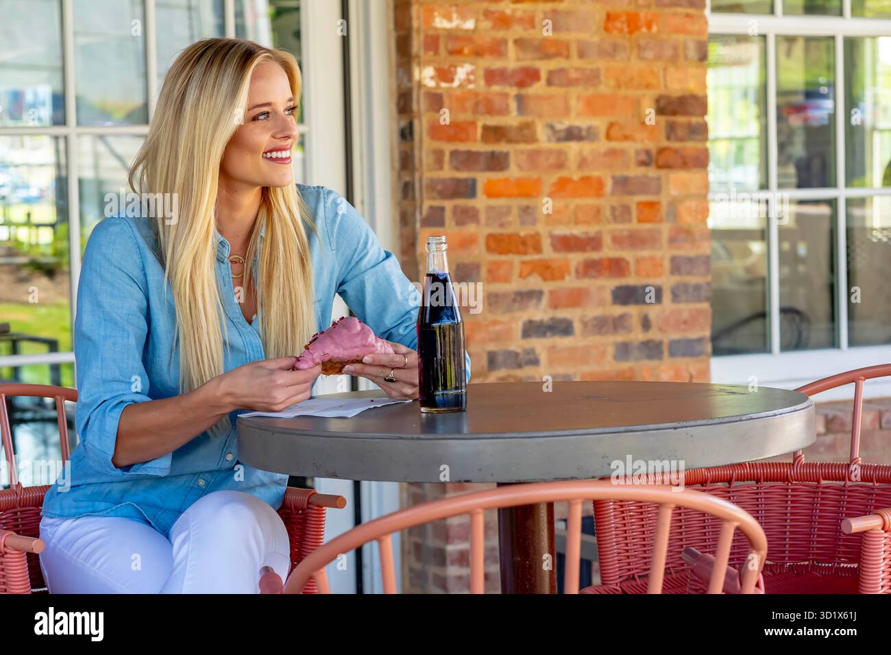 Sunlit Bliss: Schicke Blondine genießt süße Leckereien und frische Luft in der Mall Stockfoto
