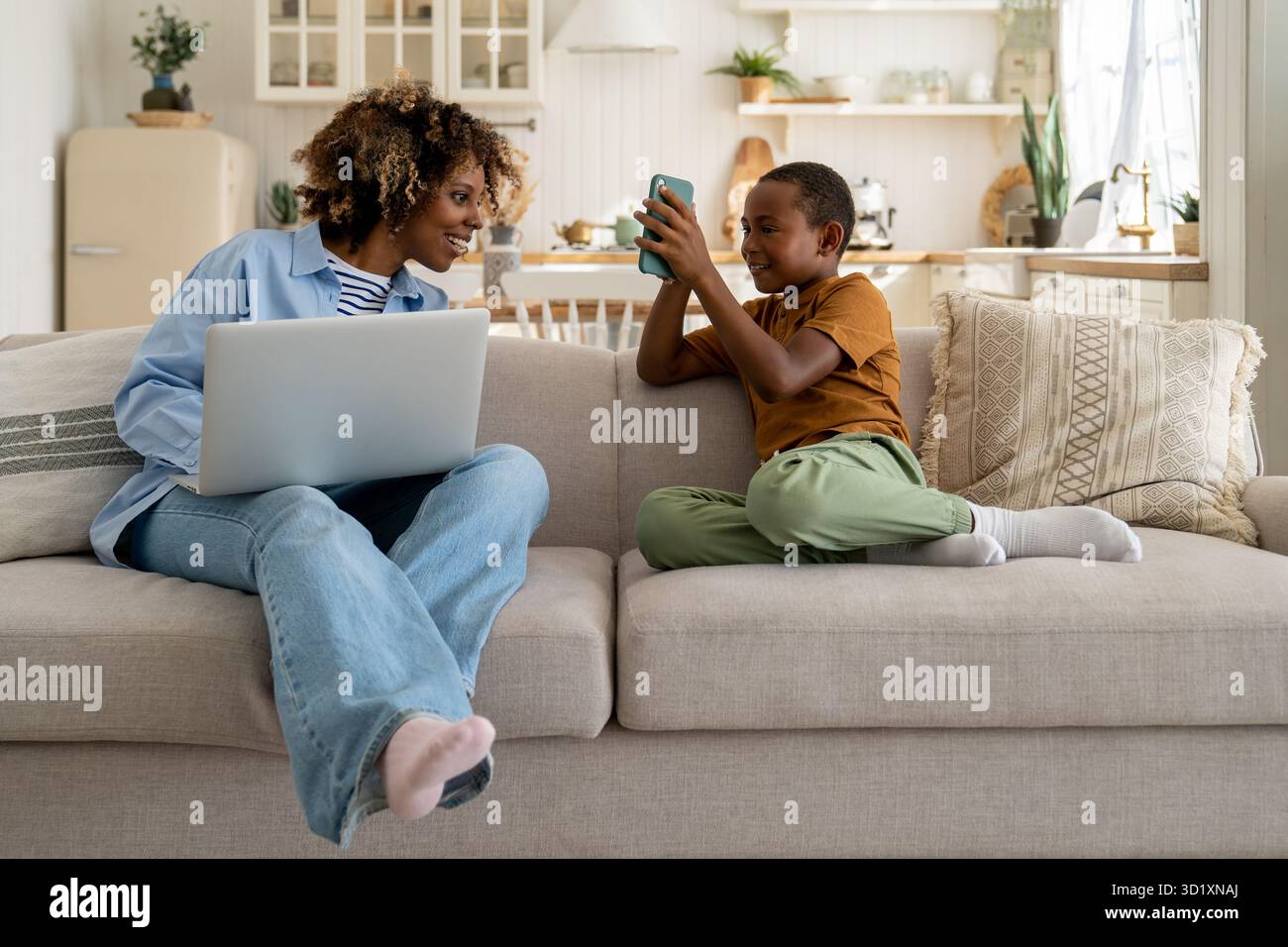 Glückliche afroamerikanische Familie, Mutter und Sohn, genießen Sie das Wochenende zu Hause, auf dem Sofa mit Geräten Stockfoto