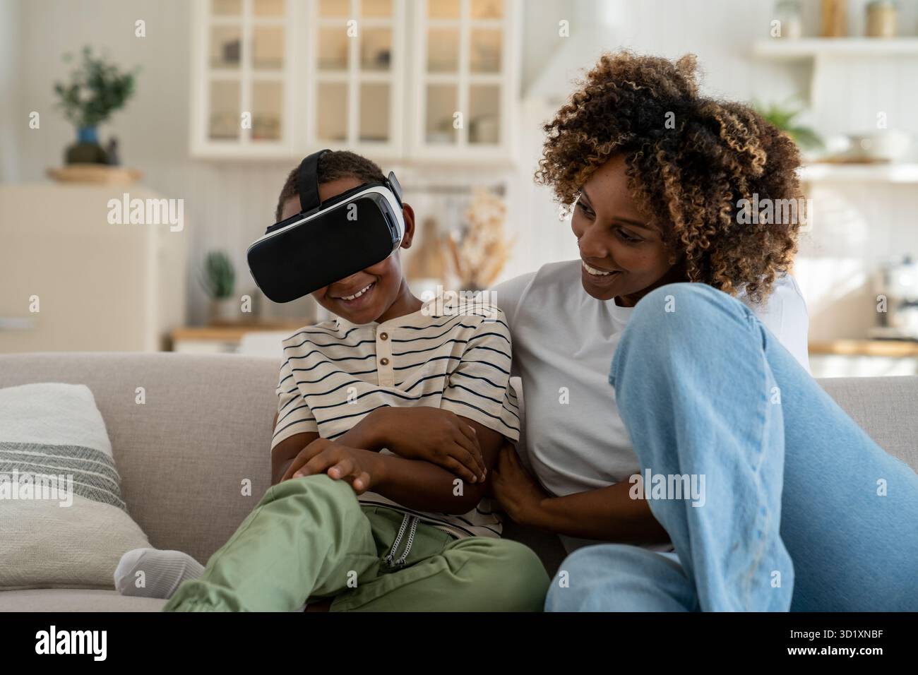 Fröhliche afroamerikanische Familie, Mutter und Sohn, die ein VR-Headset verwenden und sich auf dem Sofa entspannen Stockfoto