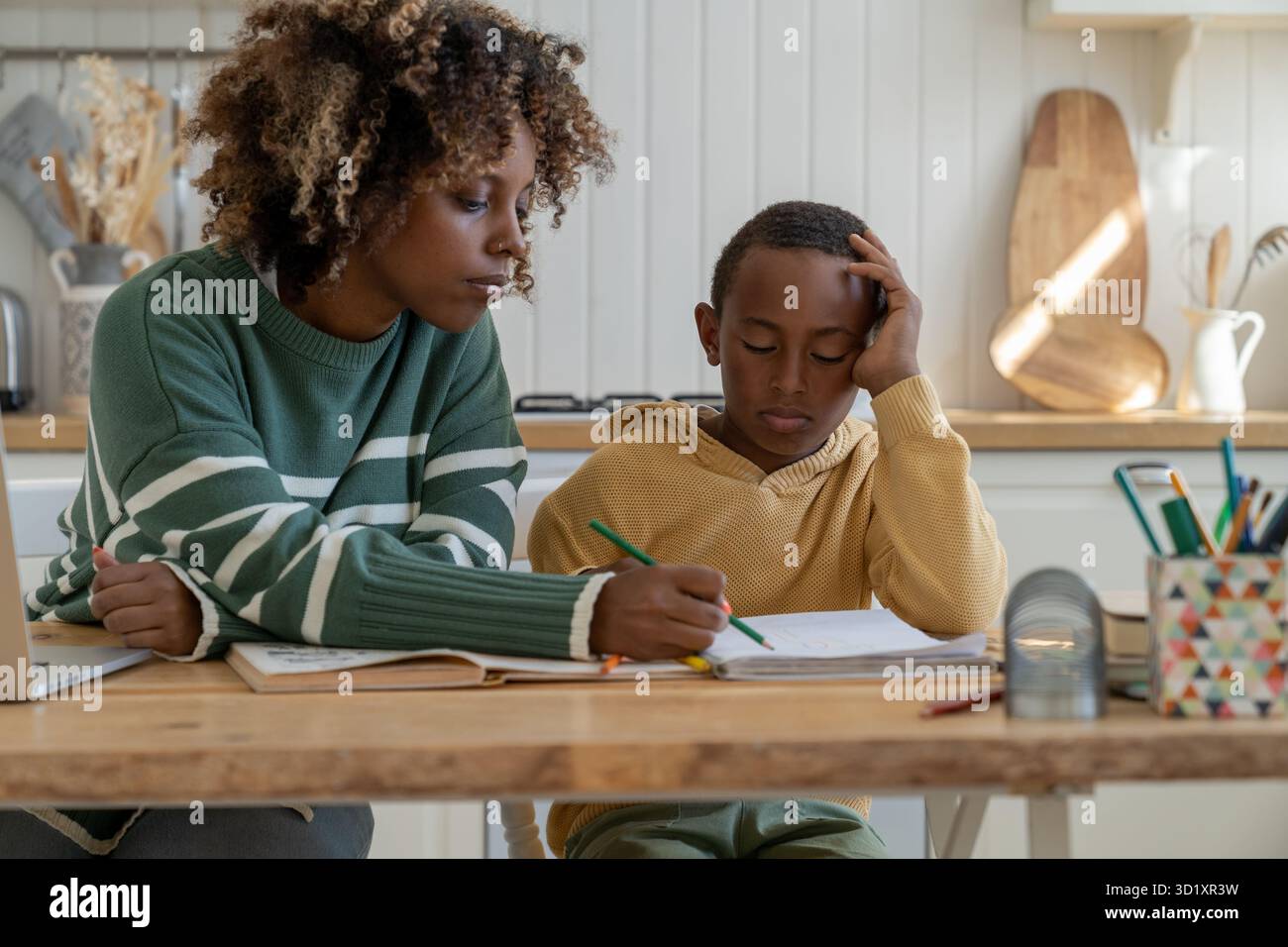 Heimunterricht für einen birassischen Schüler mit Hilfe einer Privatlehrerin. Der pensive Sohn macht Hausaufgaben mit mom Stockfoto