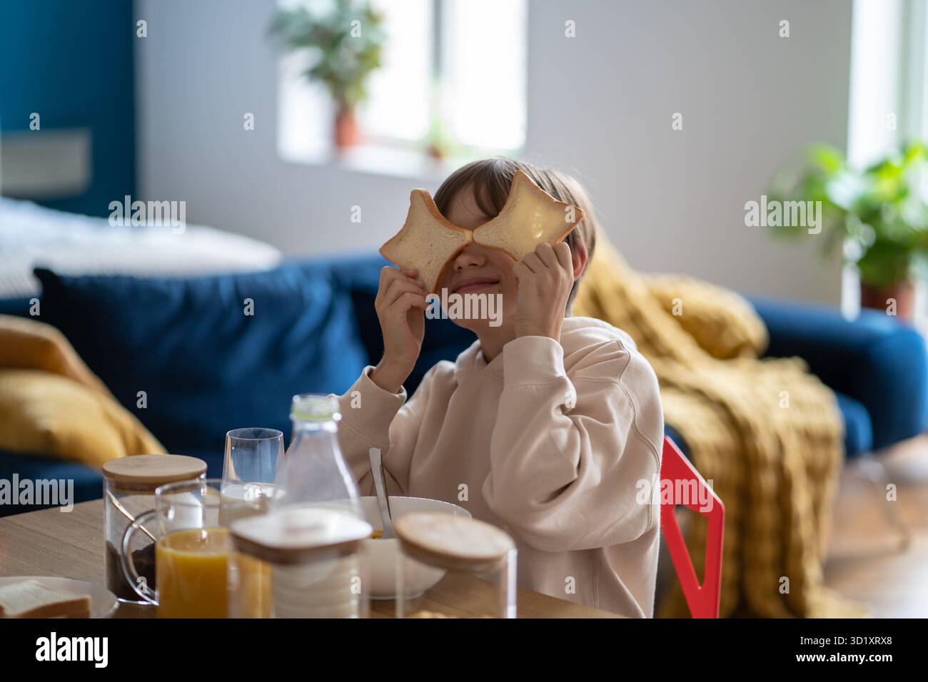 Ein kleiner Junge, der mit Brotstücken spielt, während er im Küchenheim am Tisch sitzt Stockfoto