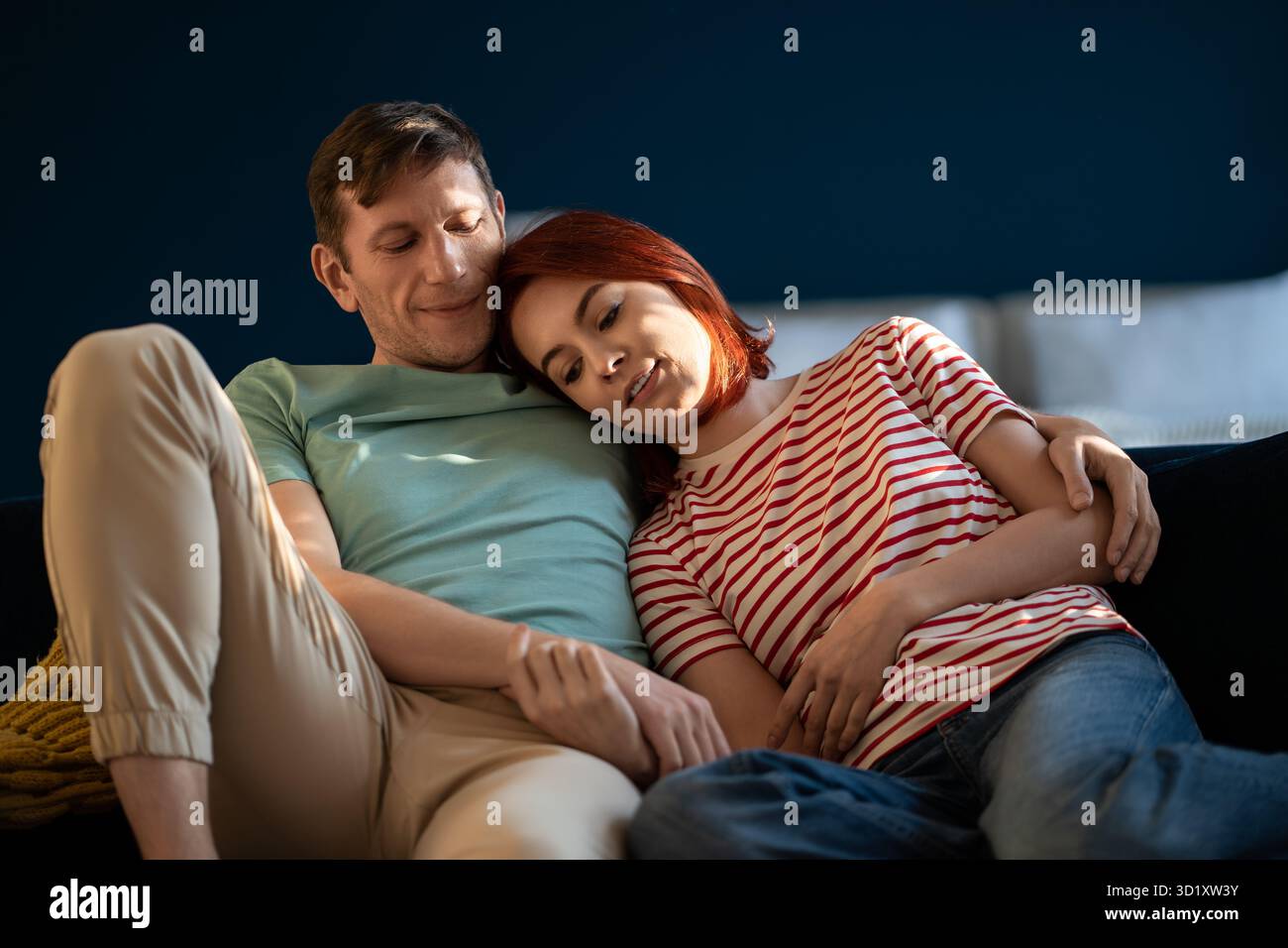 Ein verliebtes Paar, das auf der Couch sitzt und Händchen hält, sich in seiner eigenen Wohnung umarmt. Emotionale Verbindung Stockfoto