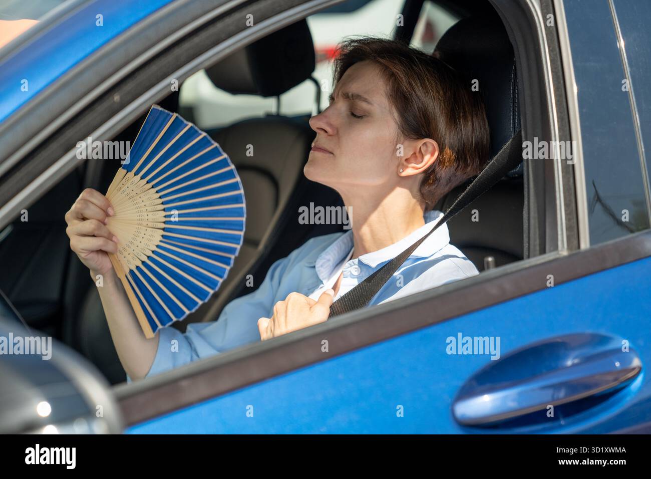Erschöpfte Frau mittleren Alters fährt Autowellen blauer Fan leidet an Stau im Verkehr. Stockfoto