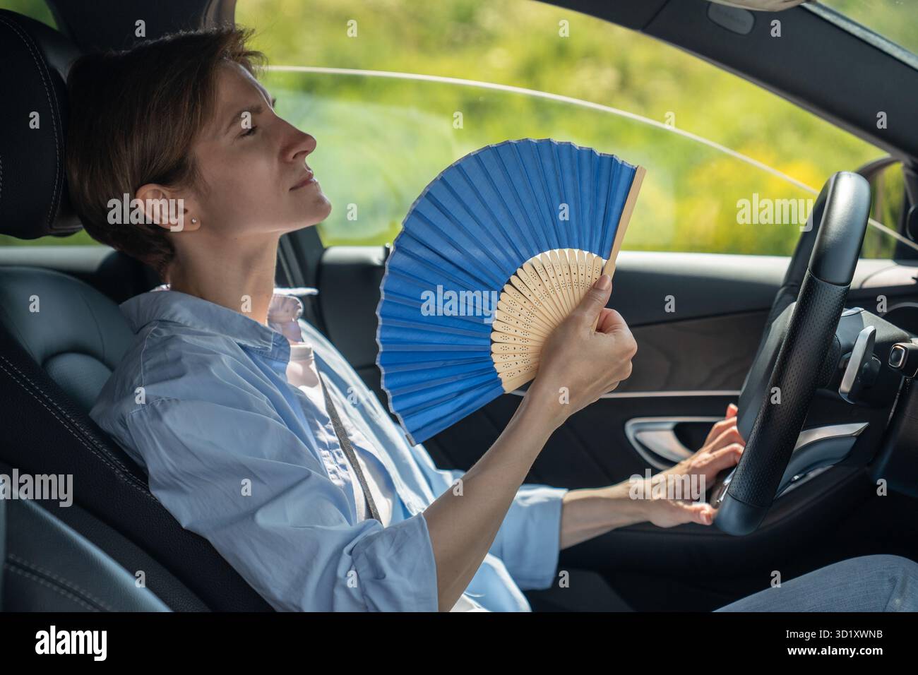Überhitzte, erschöpfte Fahrerin mittleren Alters mit Handventilator, die an Hitze im Auto leidet. Heißes Wetter Stockfoto