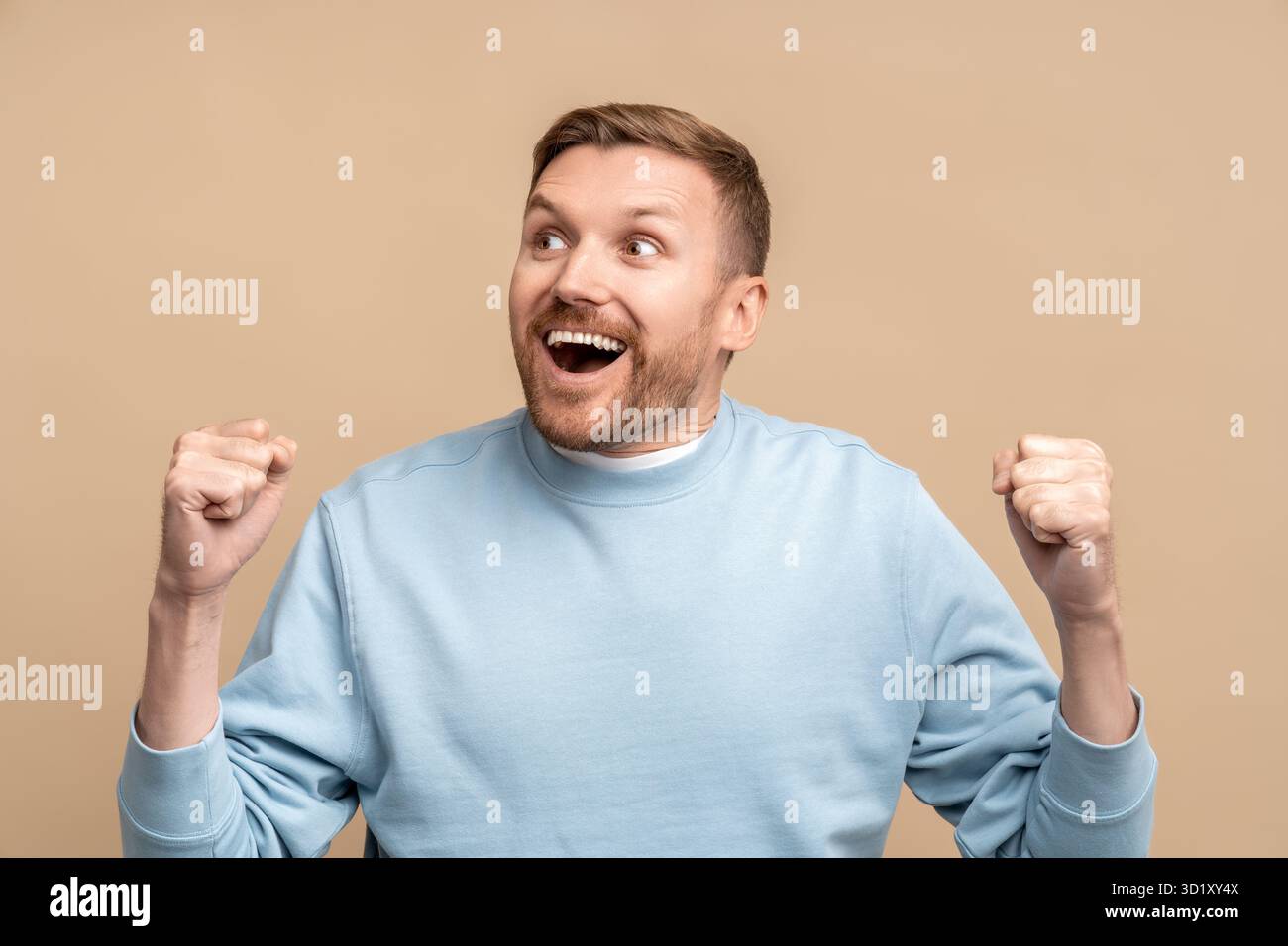 Überglücklich staunender Mann, der Siegeshand zeigt, Geste geballte Fäuste auf beigefarbenem Hintergrund. Stockfoto