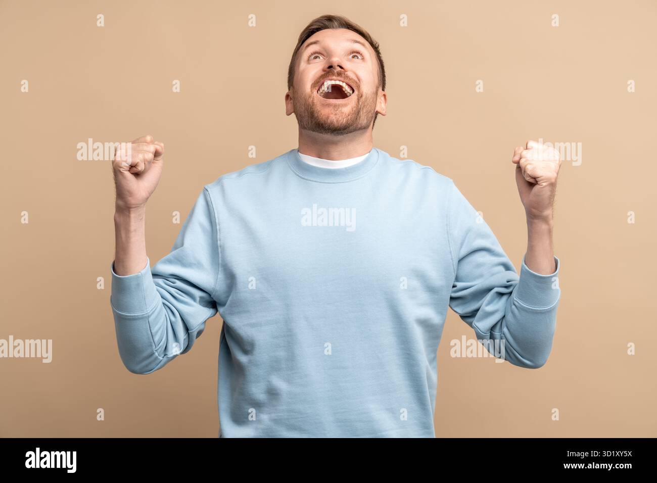 Überglücklich staunender Mann, der Siegeshand zeigt, Geste geballte Fäuste auf beigefarbenem Hintergrund. Stockfoto