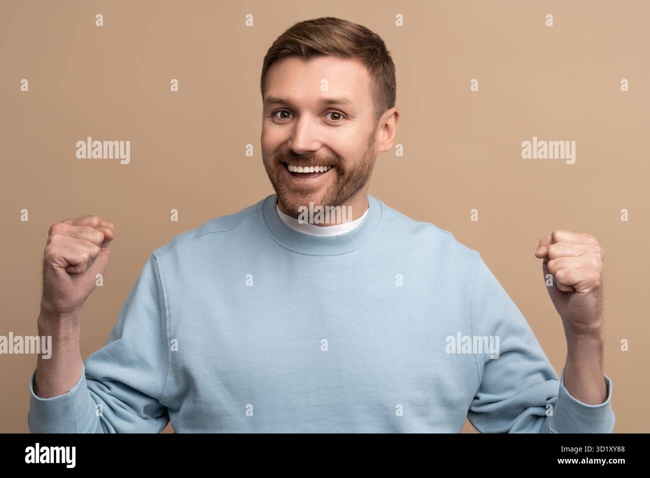 Glücklicher fröhlicher Mann zeigt Siegesgesgeste auf beigefarbenem Hintergrund und blickt in die Kamera. Stockfoto