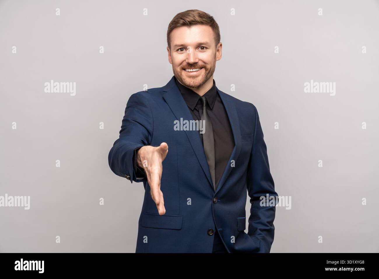 Glücklicher Geschäftsmann hält die Hand für den Handschlag und schaut auf die Kamera auf grauem Hintergrund. Stockfoto