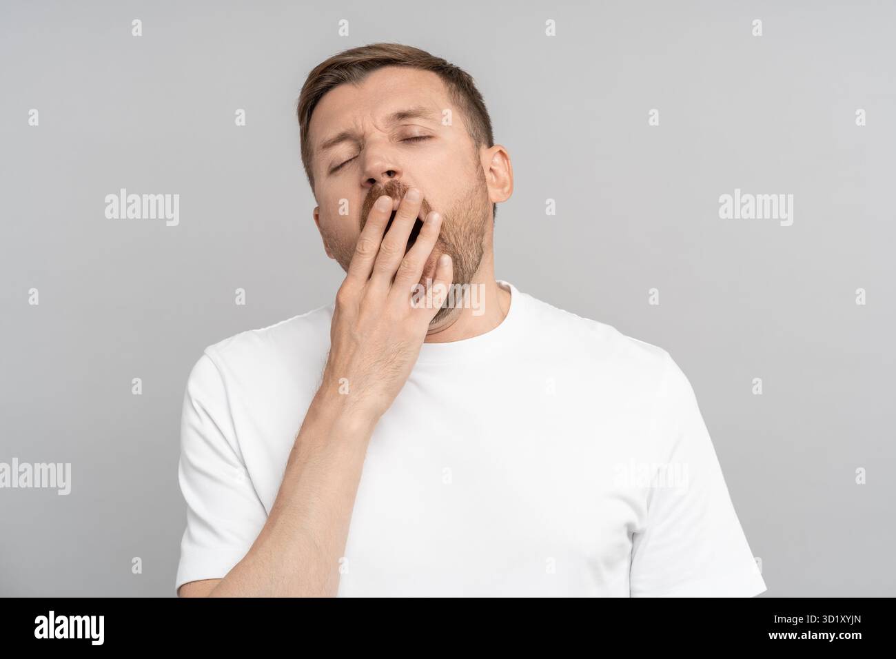 Verschlafener Gähner mit geschlossenen Augen geöffnetem Mund, der Hand auf grauem Hintergrund bedeckt. Stockfoto