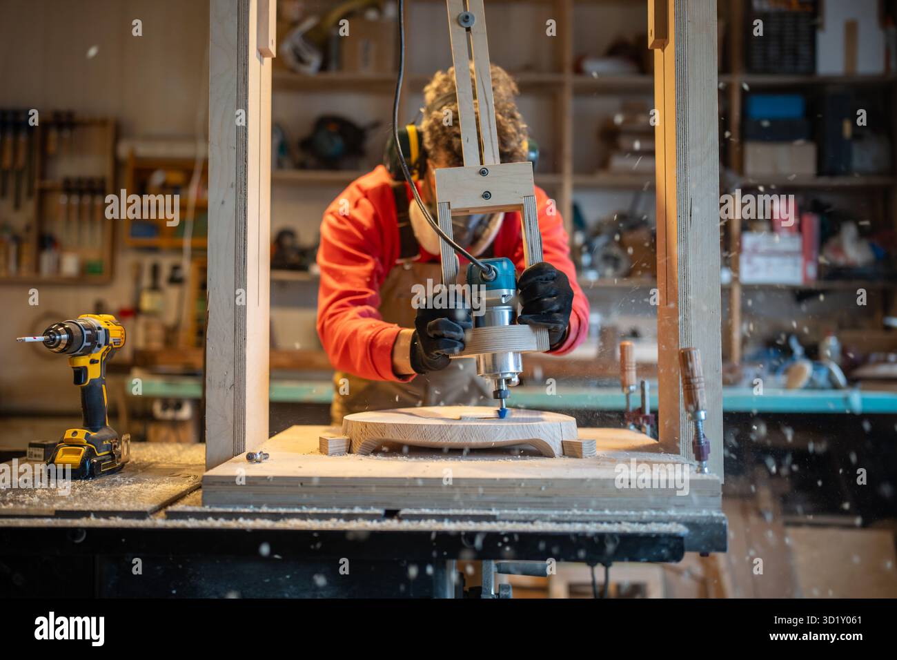 Zimmermann in Noise Cancelling-Kopfhörern, Brillen, Atemschutzmasken bohren Holzplanken in der Tischlerei Stockfoto