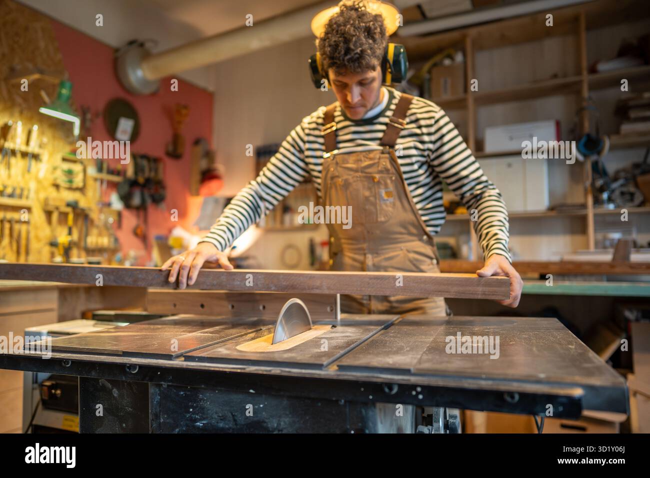 Zimmermann trägt Noise Cancelling-Sicherheitskopfhörer, Sägeplatte mit Kreissäge in Zimmerei Stockfoto