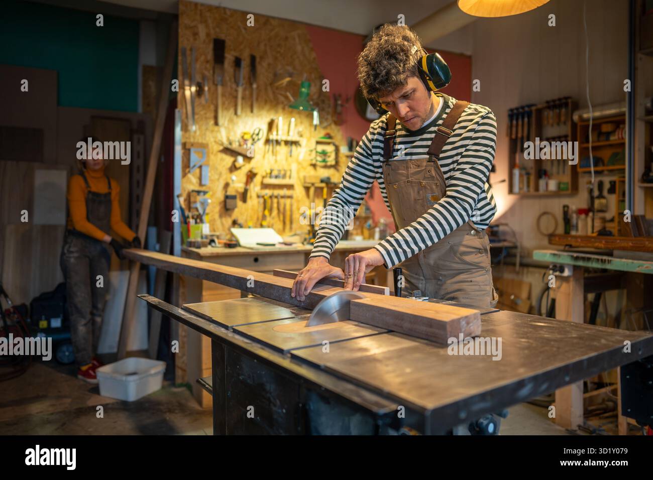 Zimmermann trägt Noise Cancelling-Sicherheitskopfhörer, Sägeplatte mit Kreissäge in Zimmerei Stockfoto