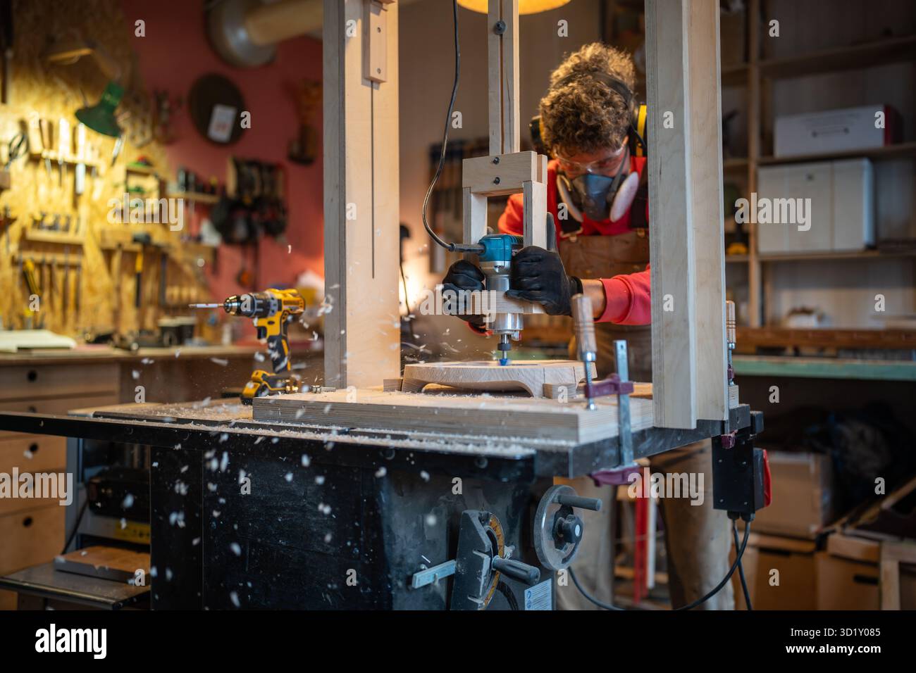 Zimmermann in Noise Cancelling-Kopfhörern, Brillen, Atemschutzgerät, das Holzdielen in der Tischlerei fräst Stockfoto